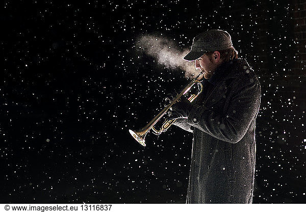 Side view of man playing trumpet during snowfall
