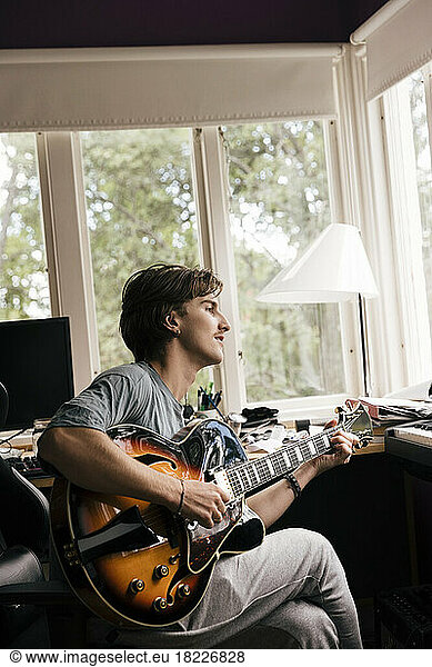 Side view of man practicing guitar while sitting at home