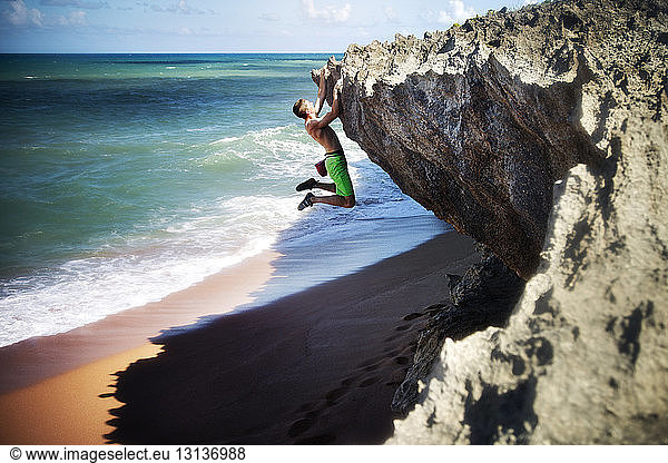 Side view of man rock climbing on beach
