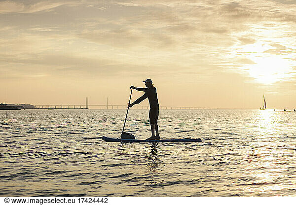 Side view of man rowing paddleboard in sea during sunset