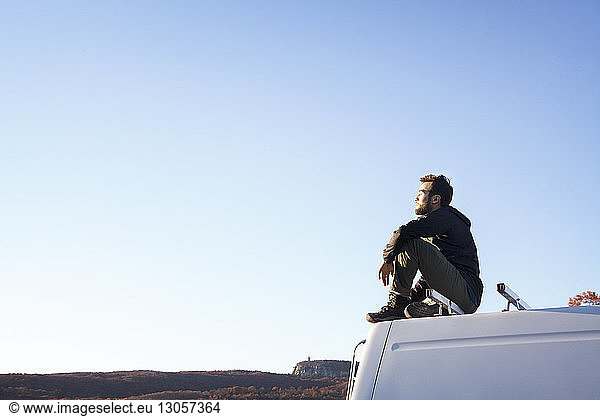 Side view of man sitting on camper van against clear sky