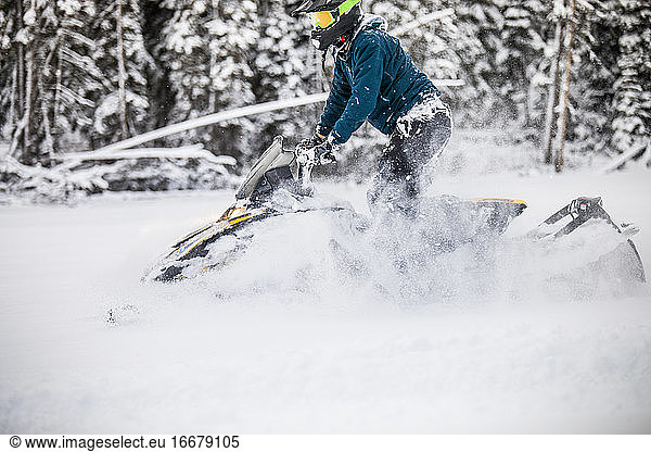 Side view of man snowmobiling through deep snow.
