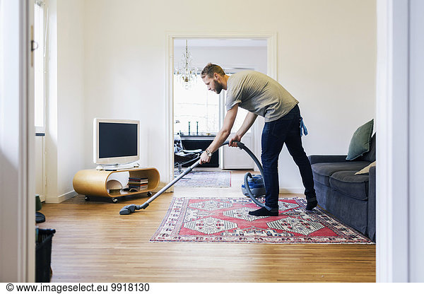 Side view of man vacuuming hardwood floor