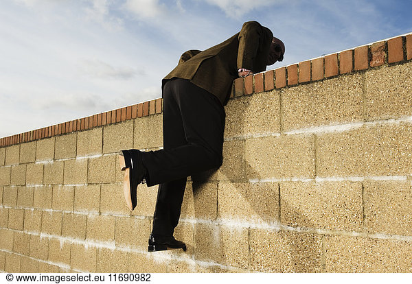 Side view of man wearing a suit climbing over yellow brick wall.