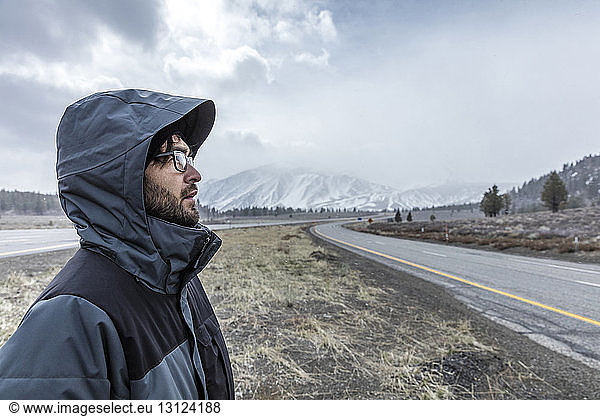 Side view of man wearing hooded jacket while standing on field against Mammoth Mountain