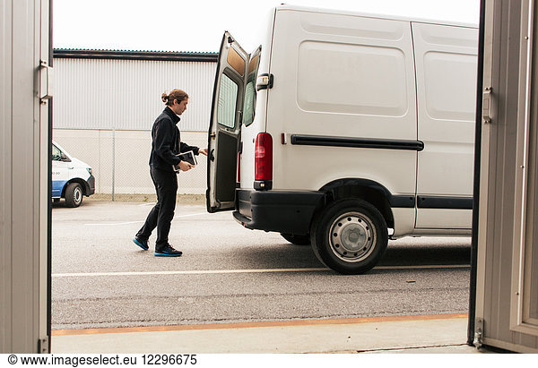 Side view of manual worker closing delivery van while standing on road