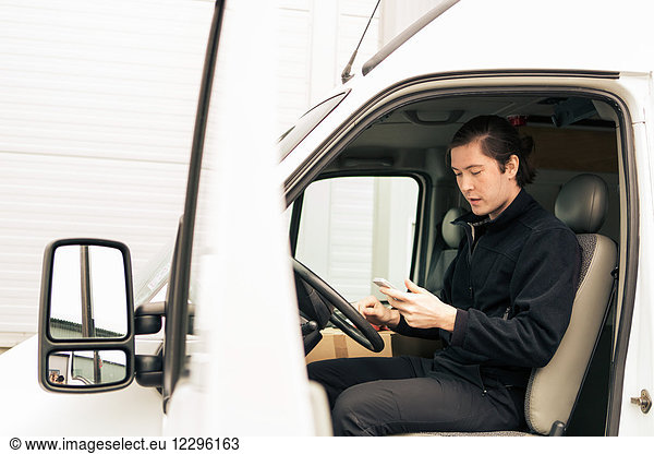 Side view of manual worker using mobile phone while sitting in delivery van