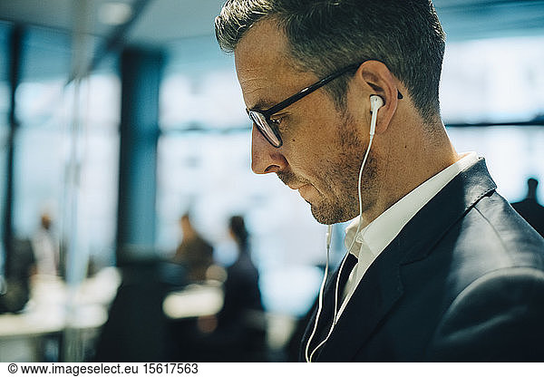 Side view of mature businessman with eyeglasses wearing headphones at office
