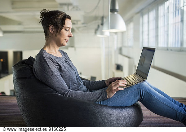 Side view of mature businesswoman using laptop while sitting on bean bag in office