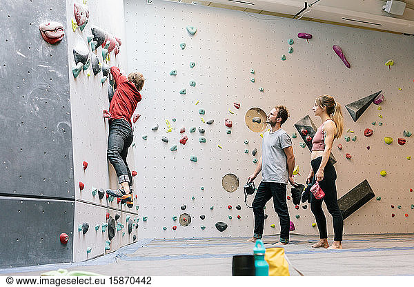 Side view of mature coach training male and female students for wall climbing in gym