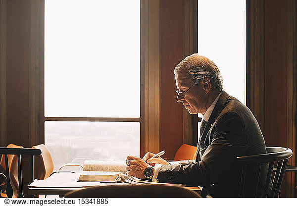Side view of mature lawyer researching while reading books at office