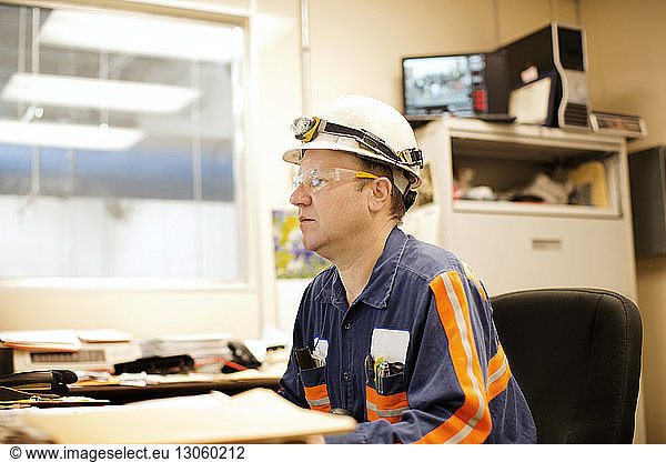 Side view of mature male worker sitting by table in recycling plant