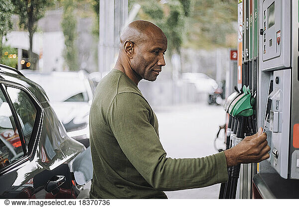 Side view of mature man doing payment through credit card while standing at gas station