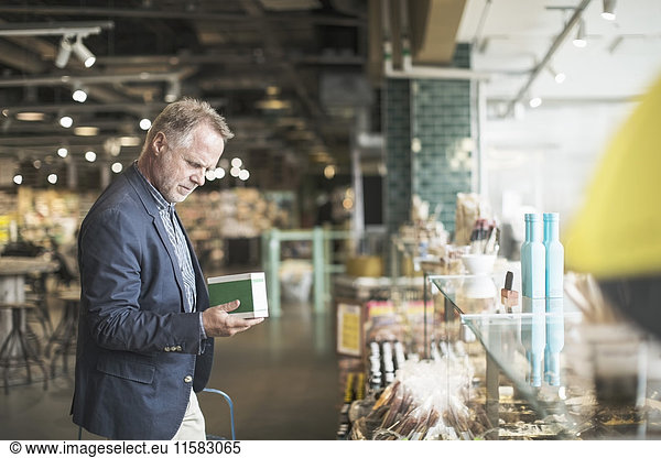 Side view of mature man reading label on food package in supermarket
