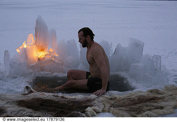 Side view of mature man taking ice bath at frozen lake during dusk
