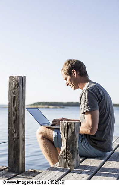 Side view of mature man using laptop on pier