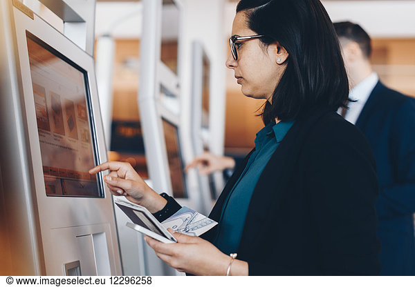 Side view of mid adult businesswoman using check in machine at airport
