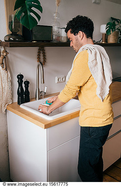 Side view of mid adult man washing utensil at sink in kitchen