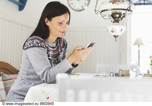 Side view of mid adult woman text messaging through mobile phone at home