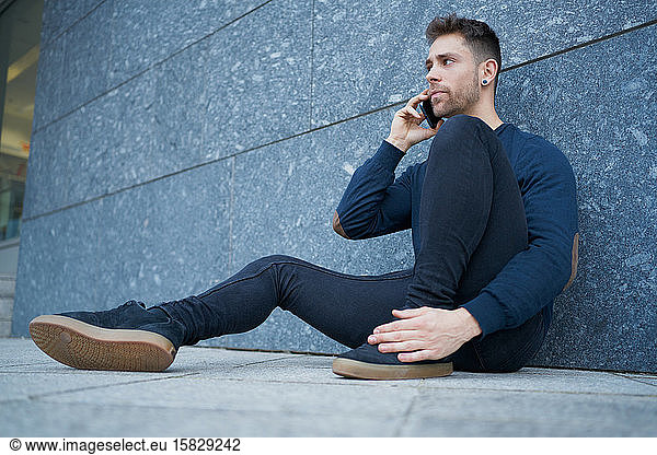 Side view of modern male in casual wear sitting near stone wall and br