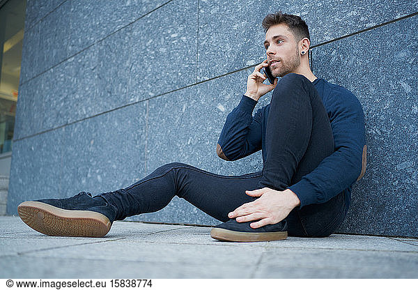 Side view of modern male in casual wear sitting near stone wall and br