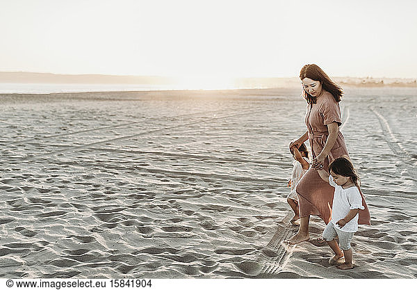 Side view of mother walking toddler twins to ocean with sun setting