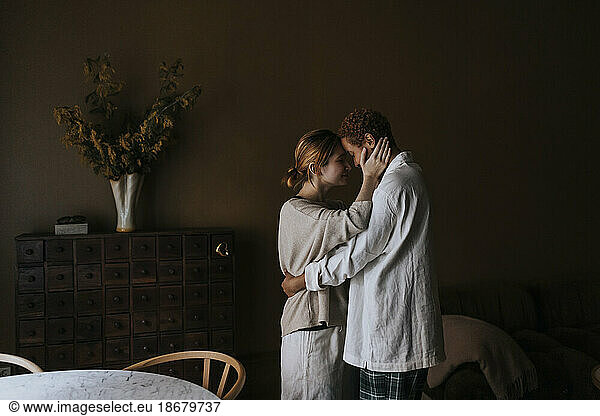 Side view of non-binary couple embracing each other at home
