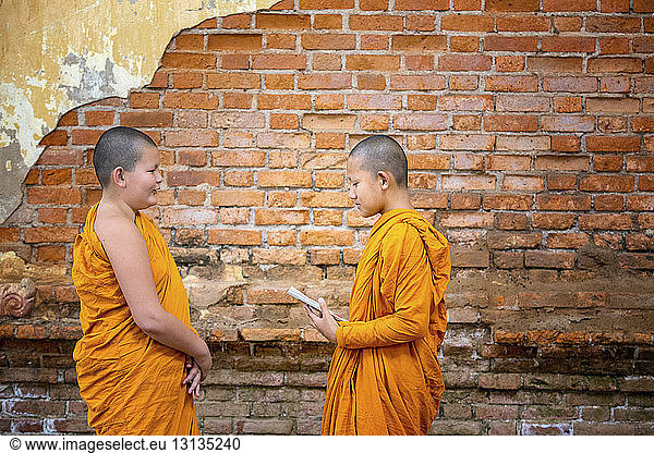 Side view of Novice Buddhist Monks studying while standing by brick wall