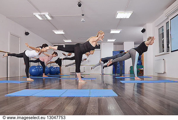 Side view of people with arms outstretched exercising on hardwood floor in pilates class