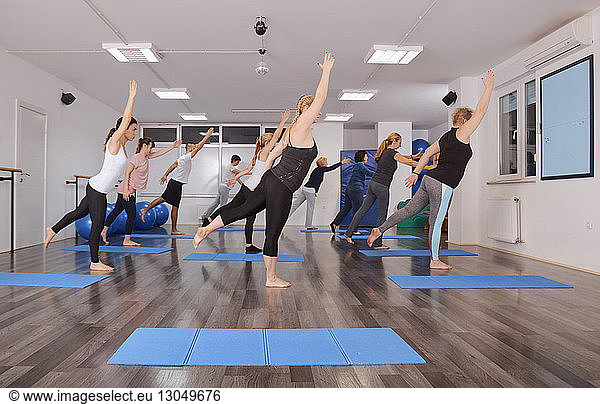 Side view of people with arms raised exercising on hardwood floor in pilates class
