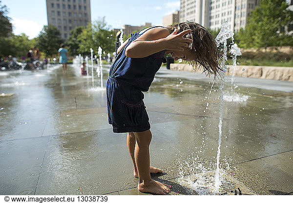 Side view of playful girl bending over fountain in park during sunny day