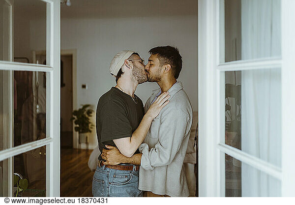 Side view of romantic gay couple kissing each other seen through doorway