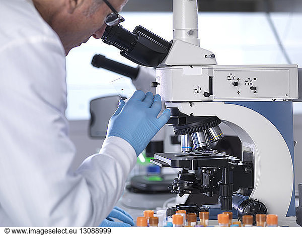 Side view of scientist analyzing blood samples through microscope in laboratory