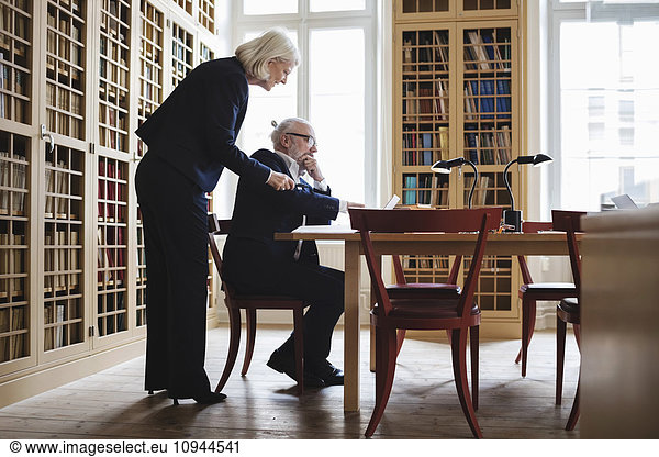Side view of senior male and female lawyer discussing at table in library
