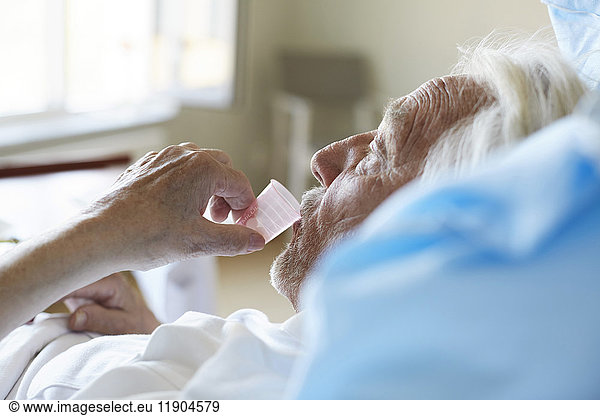 Side view of senior male patient taking cough syrup in hospital ward