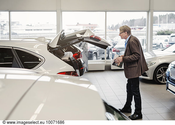 Side view of senior man examining car trunk at showroom
