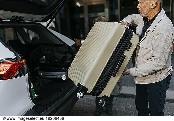 Side view of senior man loading luggage in car trunk