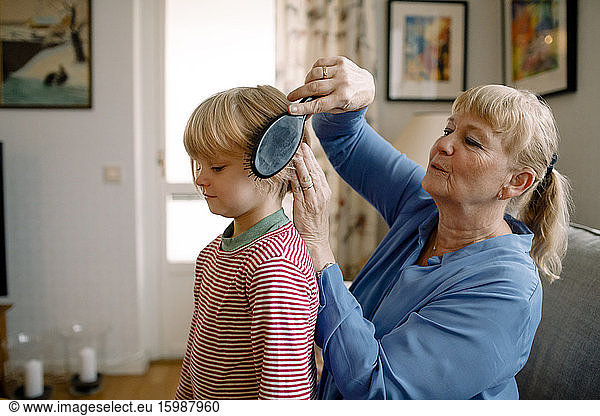 Side view of senior woman combing hair of grandson in living room at home