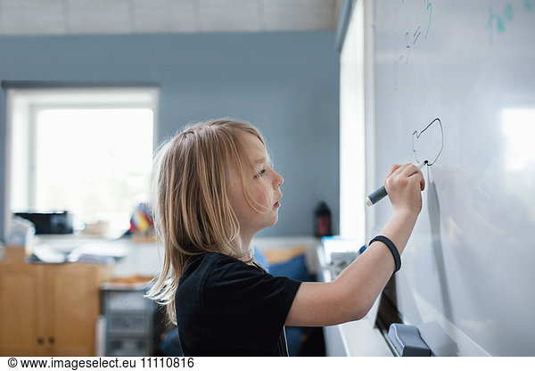 Side view of serious girl drawing on whiteboard in classroom