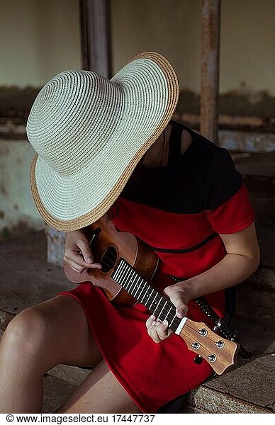 Side view of sitting girl in hat  playing ukulele  on old steps