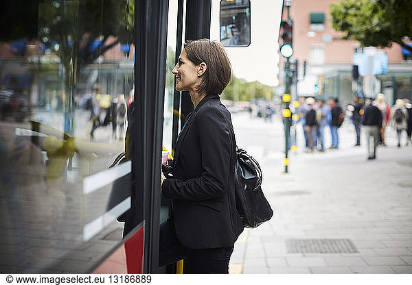 Side view of smiling businesswoman boarding bus in city