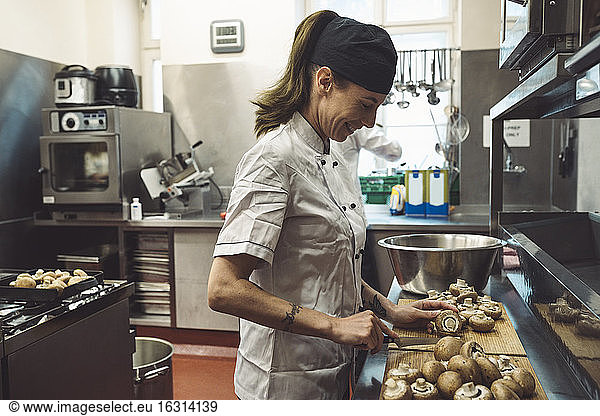 Side view of smiling female chef cutting mushrooms at kitchen counter