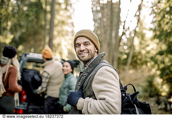 Side view of smiling man carrying backpack with friends in background
