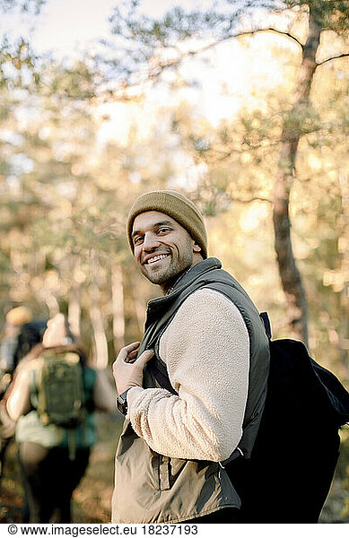 Side view of smiling man with backpack standing in forest