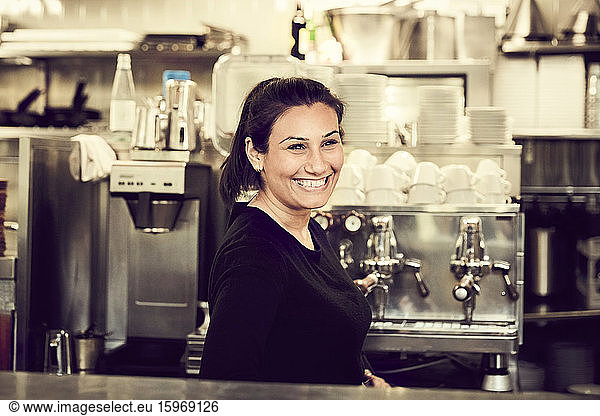 Side view of smiling owner looking away while standing at checkout counter in cafe