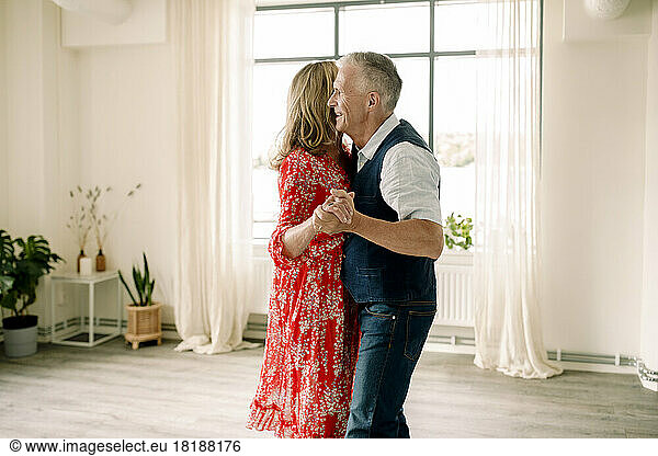 Side view of smiling senior man holding hand of woman while dancing in class