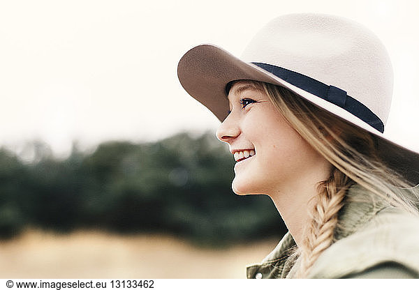 Side view of smiling teenage girl wearing hat while looking away on field