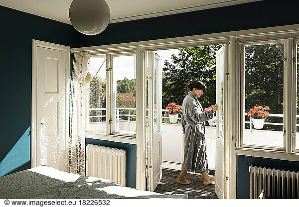 Side view of smiling woman wearing bathrobe while opening balcony door