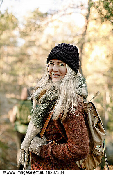 Side view of smiling young woman with backpack in forest