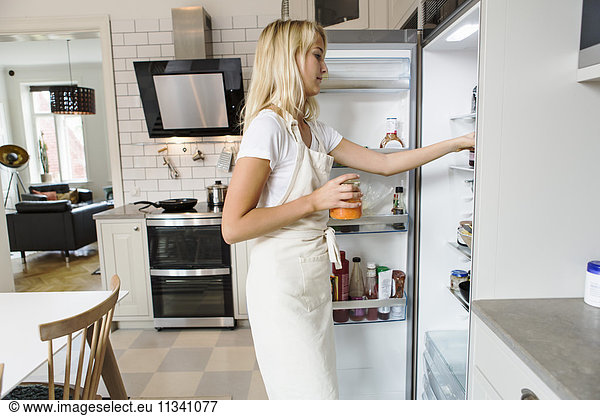 Side view of teenage girl looking in refrigerator at domestic kitchen